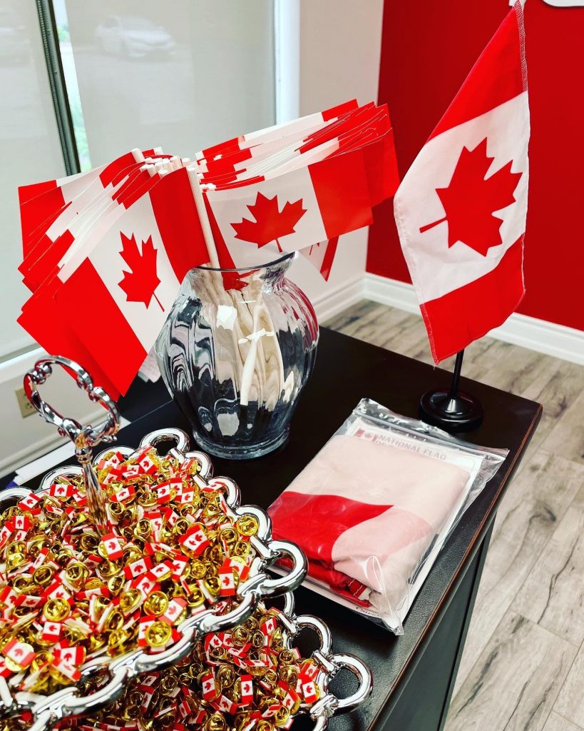 An assortment of Canadian flag materials placed on a desk including: small flags, pins, and a folded large Canadian flag.
